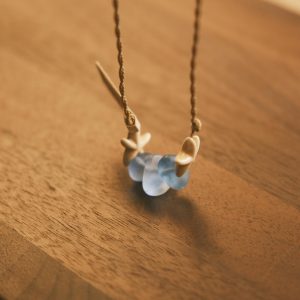 A beautiful handmade necklace featuring blue sea glass and shells on a wooden table, captured in soft light.