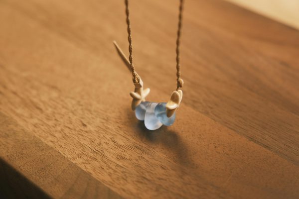 A beautiful handmade necklace featuring blue sea glass and shells on a wooden table, captured in soft light.