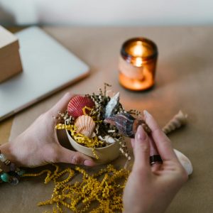 Close-up of hands creating a candle with seashells and natural elements.
