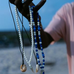 Hand holding colorful beaded necklaces on a sandy beach background.