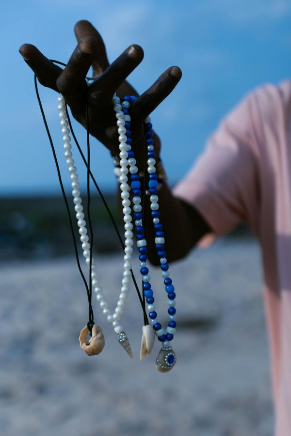 Hand holding colorful beaded necklaces on a sandy beach background.