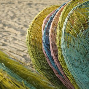 Vibrant colored wicker baskets stacked vertically on a sandy beach against a warm backdrop.