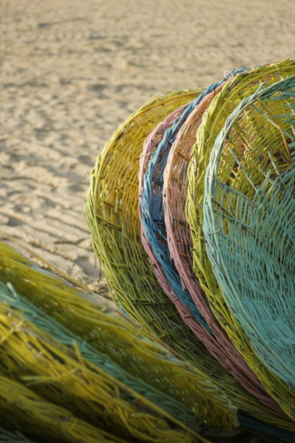Vibrant colored wicker baskets stacked vertically on a sandy beach against a warm backdrop.